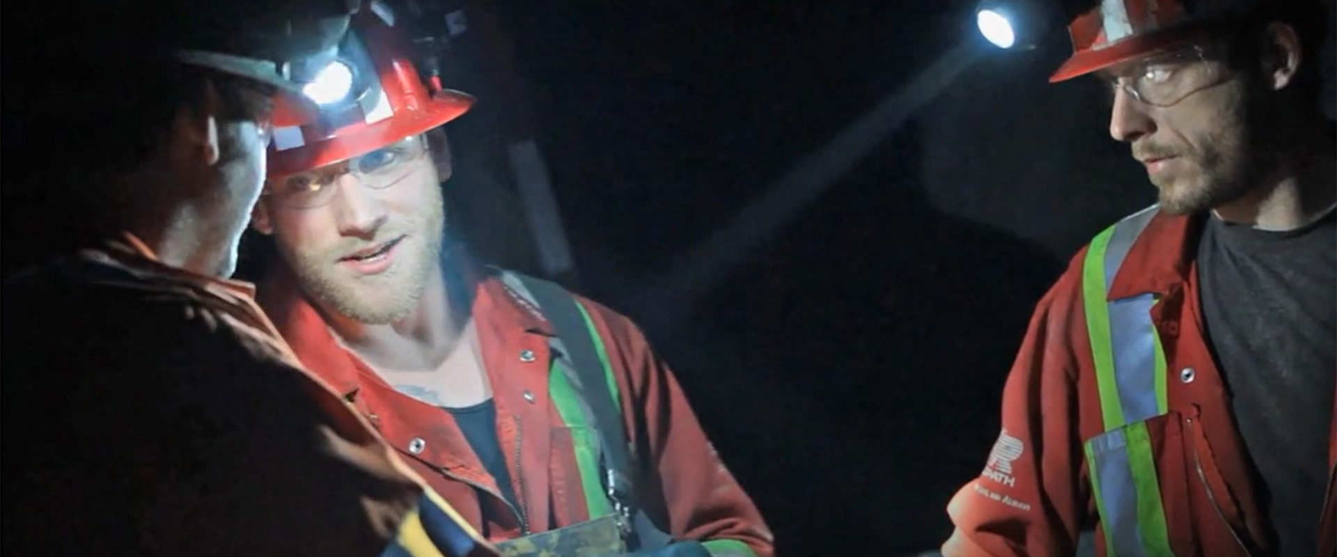 La bannière du site Web de la page sur l’accessibilité montre un groupe de mineurs de Redpath en train d’avoir une conversation dans le noir, faiblement éclairé par les phares de leurs casques de sécurité.